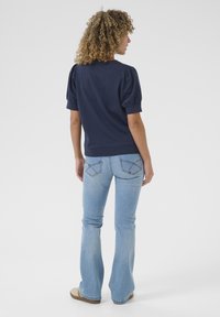 Navy blue short-sleeve top with puffed sleeves, paired with light blue flared jeans and tan shoes. Top has a rounded neckline and slim fit.