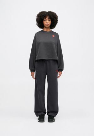 Sweatshirt court gris foncé avec un petit logo, associé à un pantalon de survêtement ample assorti et des baskets noires, offrant une texture douce.