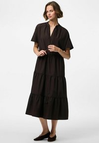 Kārtainā melnā kokvilnas kleita ar īsām piedurknēm, apaļu dekoltē un savilktu jostasvietu. Līdz ceļiem, ar mīkstu, gludu tekstūru un minimāliem akcentiem.