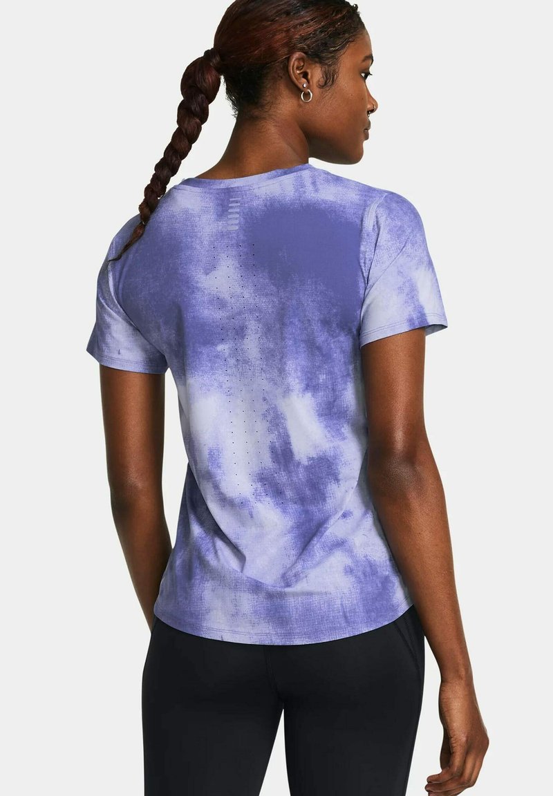 Donna con capelli intrecciati che indossa una maglietta a maniche corte viola e bianca con effetto tie-dye e pantaloni neri, vista di spalle su uno sfondo bianco.