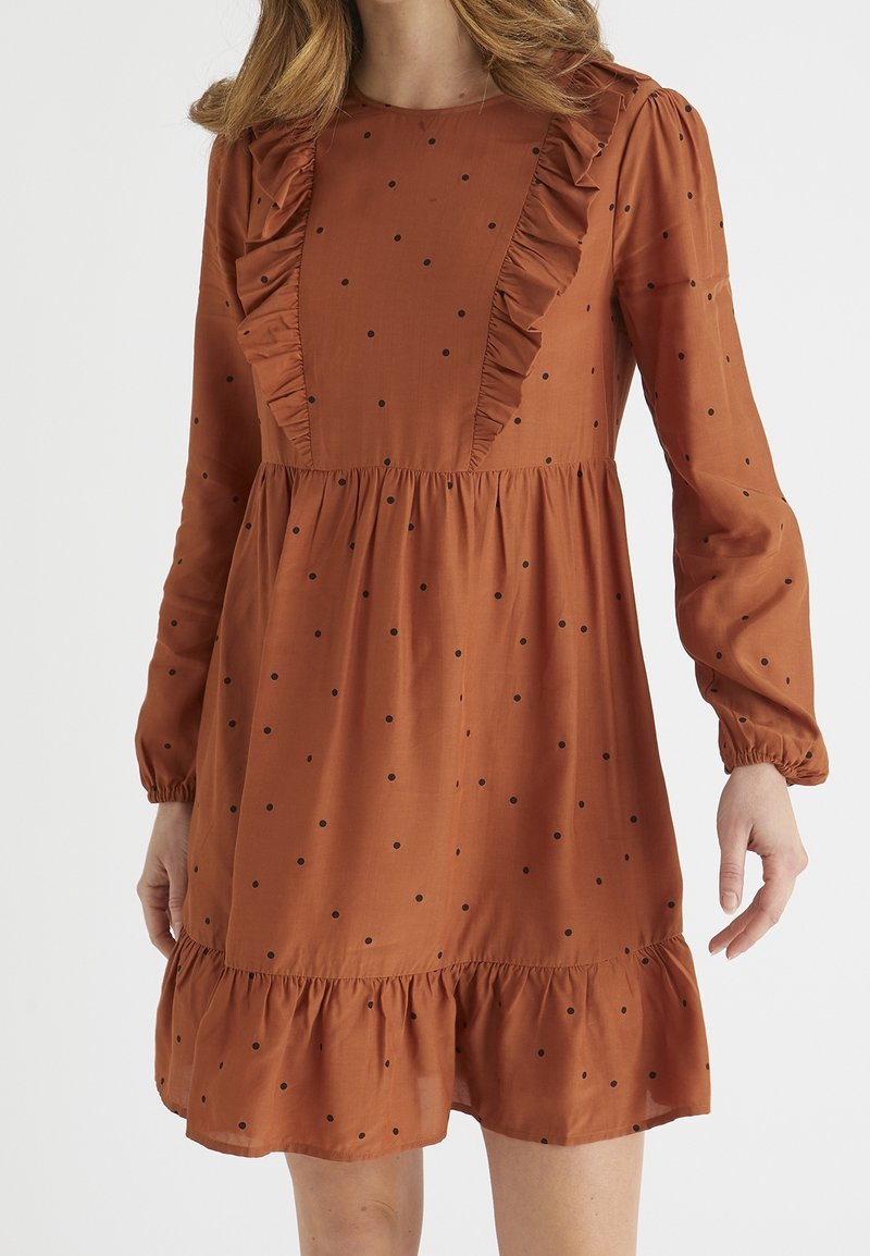 Vestido de color óxido con lunares negros, con escote y mangas con volantes, dobladillo acampanado y un ajuste holgado. Fabricado en tela suave.