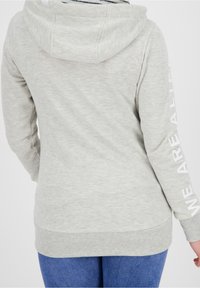 Jasnoszara bluza z kapturem o teksturowanym wykończeniu, z białym napisem „WE ARE ALIVE” na prawej rękawie. Bluza posiada kaptur i kieszeń kangurkę.