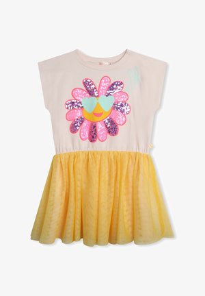 Beżowa sukienka z żółtą spódnicą tiulową, ozdobiona cekinowym kwiatem, z okularami w kształcie serca i symbolem pokoju na piersi.