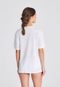 T-shirt bianco a maniche corte, leggero e leggermente trasparente, con una vestibilità comoda e un collo rotondo, visto da dietro.
