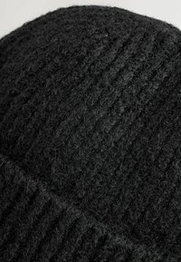 Black knit beanie with a textured pattern. Made of soft wool, showcasing a ribbed design and a slightly fuzzy finish. Round shape.