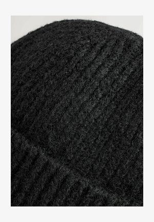 Zwarte gebreide beanie met een gestructureerd patroon. Gemaakt van zachte wol, met een geribbelde uitstraling en een licht fuzzy afwerking. Ronde vorm.