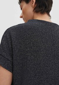 Haut en maille bleu marine avec un tissu texturé, des manches courtes et un col rond. Présente un motif subtil et une couture au dos pour plus de détails.