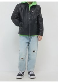 Czarna kurta z sztucznej skóry z zamkiem błyskawicznym, nałożona na jasną zieloną bluzę z kapturem. Jasnoniebieskie, postrzępione dżinsy oraz czarne trampki.