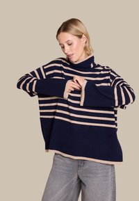 Marineblå og beige stripete høyhalset genser, laget av mykt stoff, med løs passform og brede ermer, samt en ensfarget nederkant.