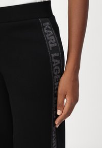 Fekete jogging nadrág, puha textúrával és rugalmas derékkal. Oldalán egy csík található fémes "KARL LAGERFELD" logóval ezüst színben.