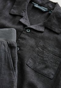 Chemise gris foncé à boutons, col, poignets côtelés, poche latérale et logo "ALLSAINTS" embossé sur la poche poitrine.