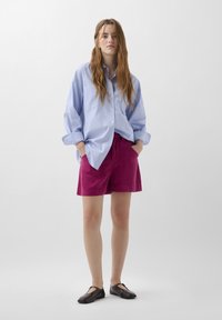 Blauw-witte gestreepte overshirt, roze shorts en zwarte instap schoenen. Stof lijkt glad; shorts hebben voorkeurszakken en een relaxte pasvorm.