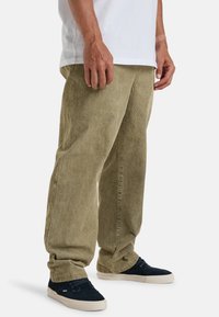 Khaki kordfløyelsbukser med avslappet passform, med vertikale ribber, mansjetter og en lett falmet tekstur. Brukt med marineblå semsket lær-sneakers.