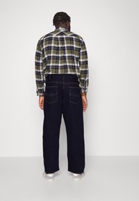 Károvaná košile na knoflíky v zelené, námořnické a bílé barvě s dlouhými rukávy; kombinována s tmavě modrými džíny z denimu s pěti kapsami a švy.