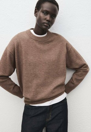Pull en maille marron avec un col rond, des poignets et un ourlet côtelés. Superposé sur un t-shirt blanc, associé à un jean en denim foncé.