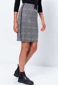 Jupe crayon à carreaux noir et blanc, longueur genou, avec une fente sur le côté et une couture noire contrastante. Assorti à des bottines en cuir noires.