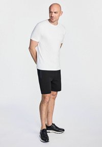 Biała bawełniana koszulka i czarne szorty z niebieskim paskiem, w połączeniu z czarnymi butami sportowymi. Styl jest casualowy i sportowy.