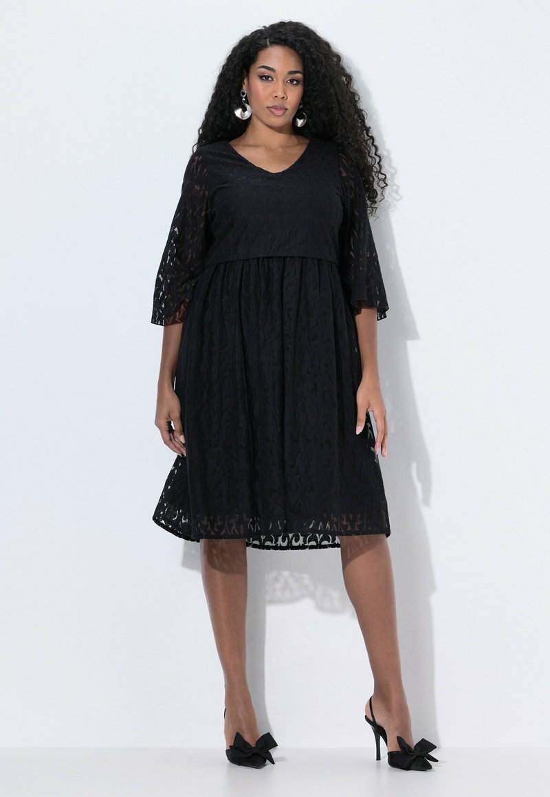 Abito in pizzo nero con scollo a V, maniche a tre quarti e gonna svasata. Presenta un motivo floreale e un design con vita stretta.