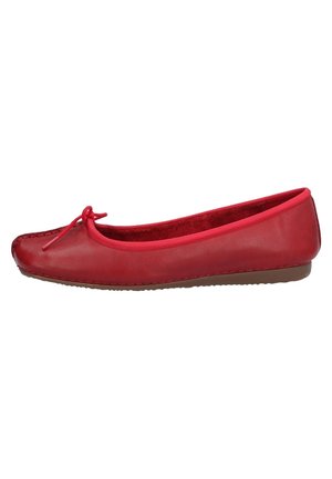 Rød ballerina med sløjfe på toppen, rund tå og flad brun sål, vist i sideprofil på hvid baggrund.