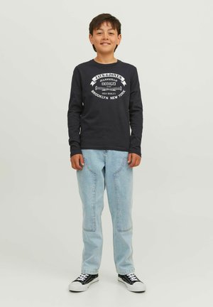 Camicia a maniche lunghe blu navy con testo e grafica bianchi, abbinata a jeans in denim azzurro chiaro con cuciture a contrasto e sneakers nere.