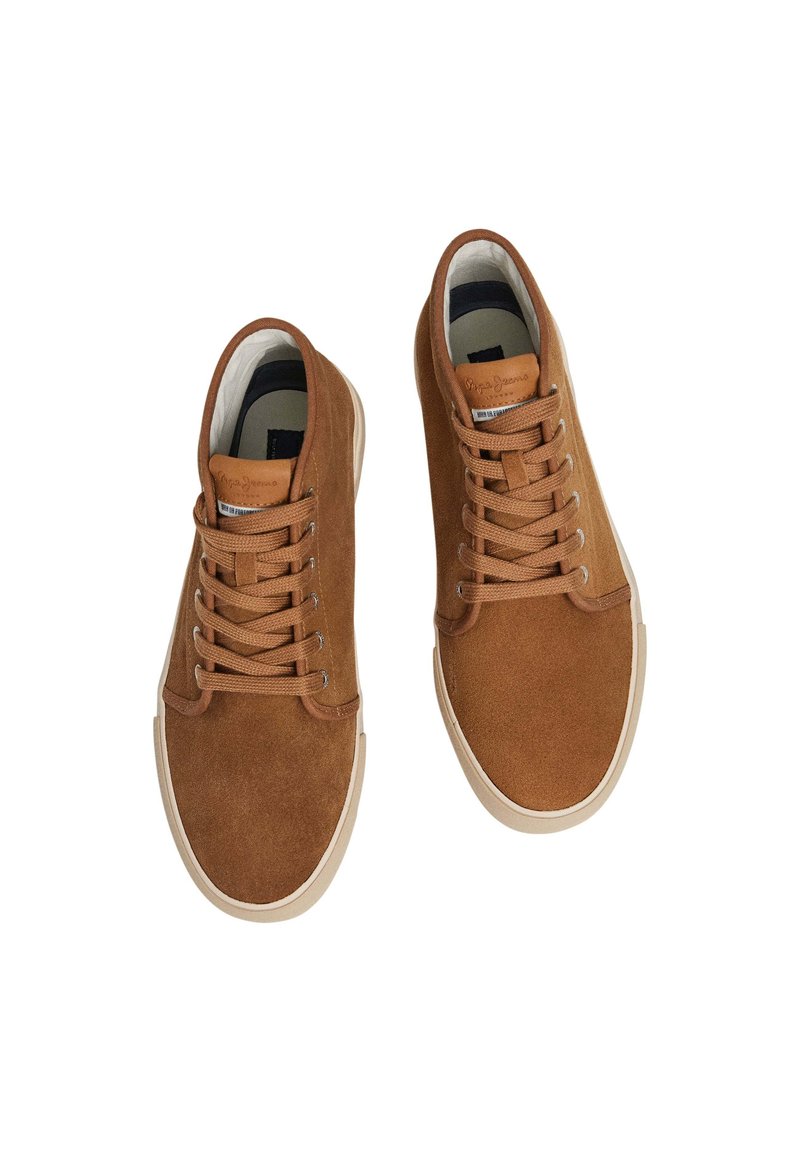 Zapatillas de ante marrón con suelas de goma crema, punta redonda y seis ojales. Cuenta con cordones planos y una etiqueta de cuero con la marca en la lengüeta.