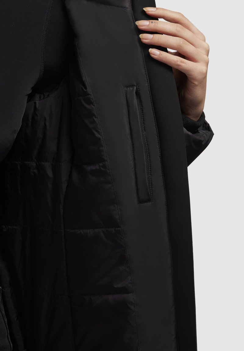 Schwarze Pufferjacke innen mit glatter, glänzender Textur; verfügt über eine senkrechte Tasche auf der linken Seite und ein kontrastierendes mattes Äußeres.