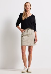 Beige katoenen rok met een rechte snit, voorzien van voorzakken en een knoopsluiting. Gecombineerd met een zwart shirt met lange mouwen en witte sneakers.