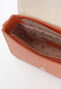 Borsa in pelle arancione con texture e scomparto con zip, caratterizzata da una fodera interna beige e una tasca con zip aggiuntiva per l'organizzazione.