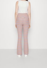 Sittande, flerfärgade utsvängda byxor med vertikala ränder i rosa, orange och lila. Elastisk midja, mjukt tyg med ribbad struktur.