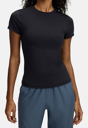 Woman wearing a fitted black short-sleeve t-shirt and loose blue pants, standing with arms relaxed by sides.