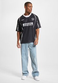 Juoda trumpomis rankovėmis marškinėliai su baltais akcentais ir logotipu, derinami su šviesiai mėlynomis plačiomis kelnėmis ir baltomis sportbačiais. Paprastas sportinis dizainas.