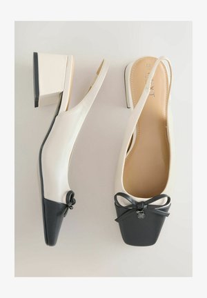 Aukštakulniai su dirželiais ant kulno, balto viršaus ir juodo kvadratinio bato priekinės dalies. Juose yra kaspino detalė ir stulpelio formos kulnas, derinantys lygų ir tekstūruotą odą.