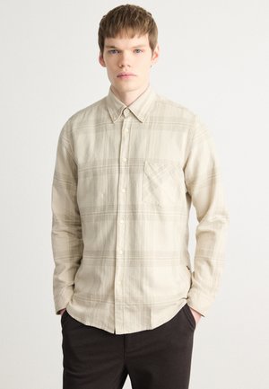 Camicia a quadri beige con bottoni, maniche lunghe, tasca sul petto e vestibilità comoda. Tessuto morbido con una leggera texture e accenti marrone chiaro.