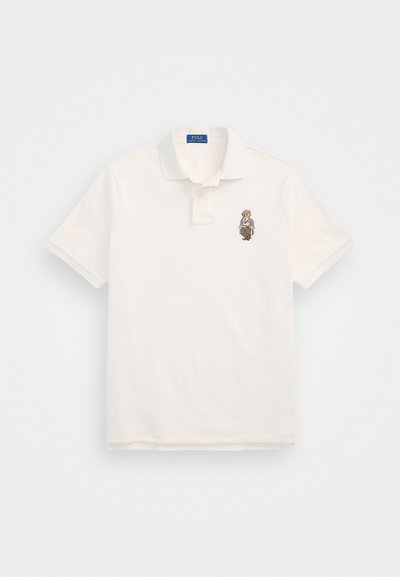 Bela polo majica iz bombaža, z dvema gumboma na ovratniku in vezanim motivom medveda na levem prsnem delu. Klasičen kroj.