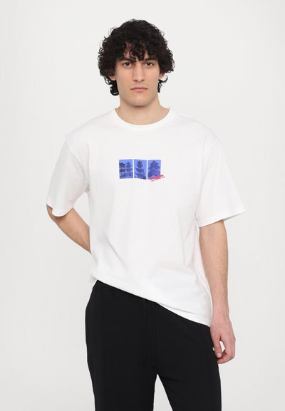 T-shirt blanc à manches courtes avec un design graphique bleu comportant trois images de structures et un texte rouge au centre.