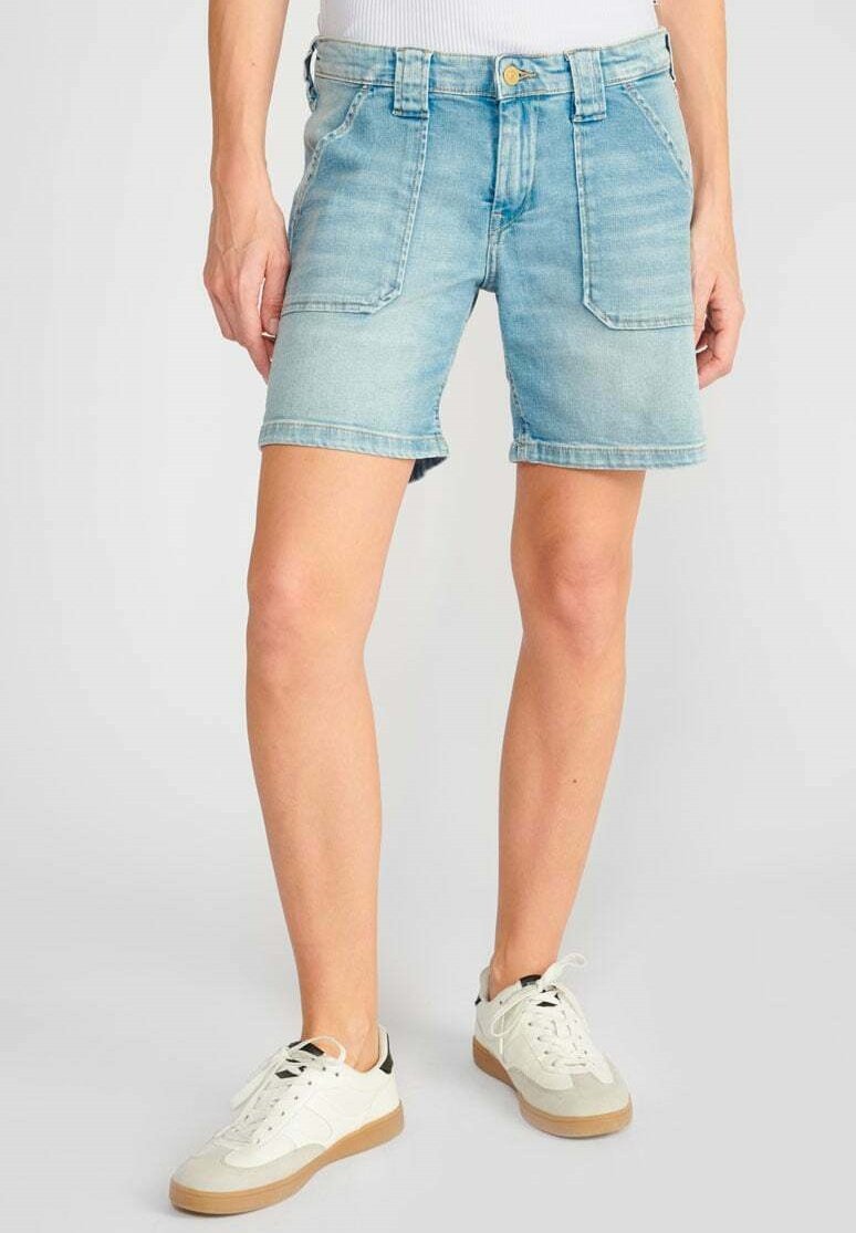 Shorts en denim bleu clair avec un délavage, dotés de poches avant, d'une fermeture à bouton et d'un ourlet roulé. Associés à des baskets blanches.