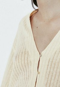 Lichtgele cardigan met een geribbelde textuur, met een diepe V-halslijn en twee knopen aan de voorkant, gemaakt van een zachte, lichtgewicht stof.