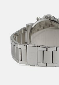 Montre en métal argenté avec un bracelet en acier inoxydable. Présente une finition polie, des maillons rectangulaires et un mécanisme de fermoir simple.