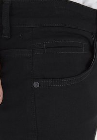 Jeans de mezclilla negra con una textura suave, que presentan un corte recto, costuras visibles y un acento de botón en el bolsillo.