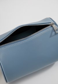 Pochette in ecopelle blu con zip argentata. Forma rettangolare arrotondata e superficie liscia, con cuciture visibili lungo i bordi.