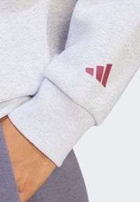 Světle šed�á mikina s žebrovanými manžetami, na levém rukávu s vínovým logem se třemi pruhy. Měkká, texturovaná látka.