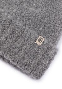 Gray knitted wool hat with a looped texture and a small beige tag featuring a black emblem and text.