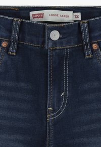 Jeans Levi's a gamba larga in denim blu scuro. Presentano rivetti in rame, cuciture gialle e una chiusura a bottone con un'etichetta sulla vita.