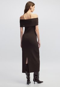 Braunes schulterfreies, geripptes Kleid mit einem seitlichen Schlitz, figurbetontem Schnitt und glatter Textur. Knielange, glänzende braune Stiefel.