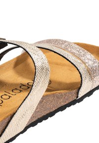 Metallisk silverfärgade sandaler med två glittrande remmar och en korkfotbädd. Texturerat mönster på remmarna; svart gummiyttersula.