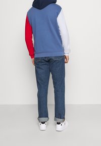 Color-blocked hooded sweatshirt with blue, red, white sleeves; cotton fabric. Paired with blue denim jeans and white sneakers.