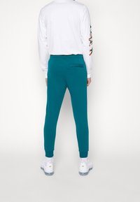 Tealfärgade joggers med en tapered passform, elastisk midja, en bakficka och muddar. Kombinerad med en vit långärmad skjorta med färggrafik.