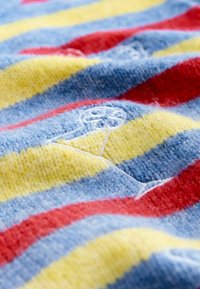 Mnohobarevná pletenina s červenými, žltými a modrými pásmi; mäkká textúra; obsahuje vyšívané detaily v svetlomodrej farbe.