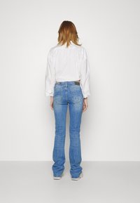 Vaqueros acampanados de color azul claro con una textura de denim, que presentan un diseño clásico de cinco bolsillos y una cintura de altura media, combinados con una camisa blanca de cuello.