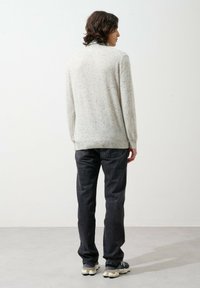 Jasnoszary sweter dziany z nakrapianym wzorem, kontrastowymi ściągaczami, w połączeniu z ciemnoniebieskimi dżinsami i czarnymi sneakersami.